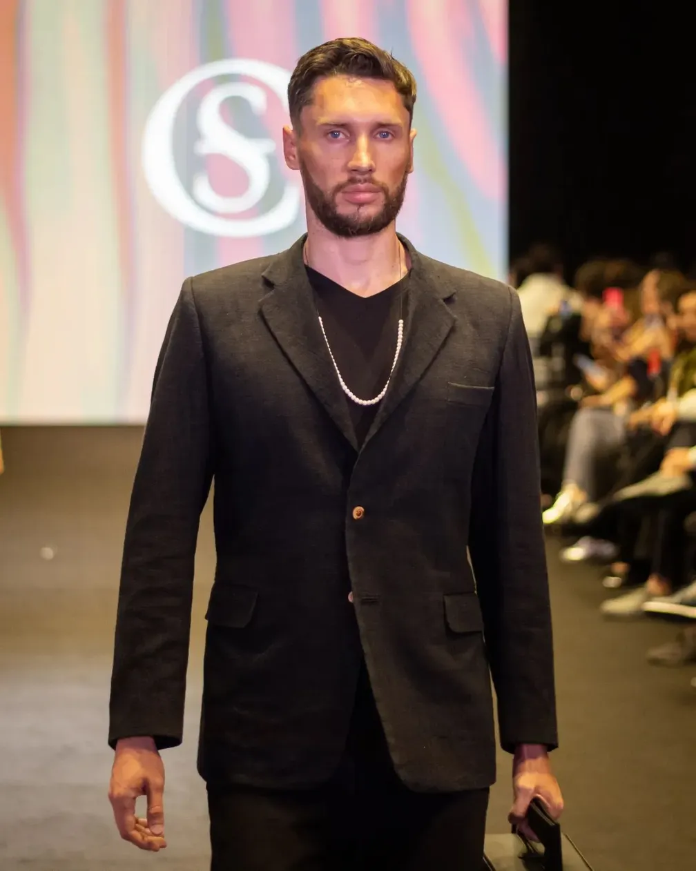 Hombre con traje negro y playera en pasarela o evento de la agencia de modelos.