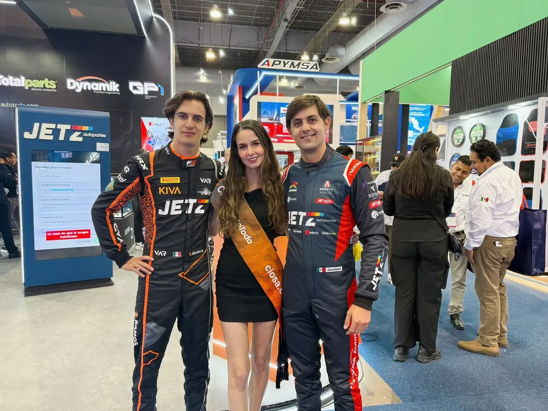 Grupo de personas y pilotos con uniformes de carreras en evento automovilístico de la agencia.